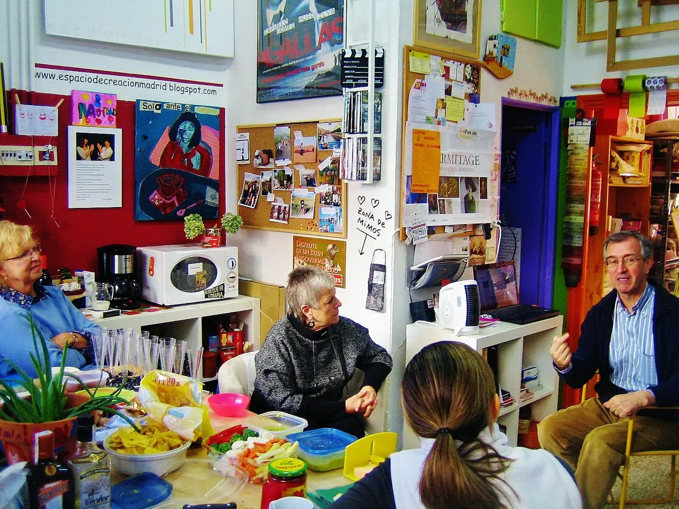 Interior del taller de Espacio de Creación: paredes cubiertas de cuadros y dibujos, ambiente policromo y bohemio, rincón de café y puerta pintada de colores.